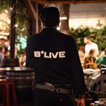 B*LIVE waiter with the logo on the back of his shirt standing near performer